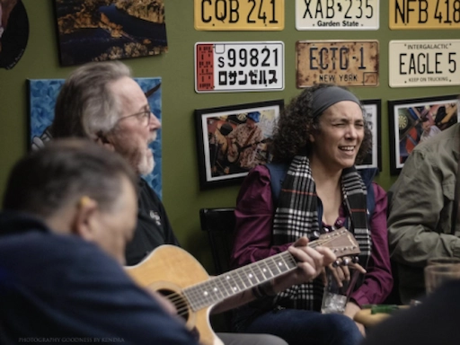 An interior action shot at the Forum Pub during a community jam session with a man playing guitar and a woman singing